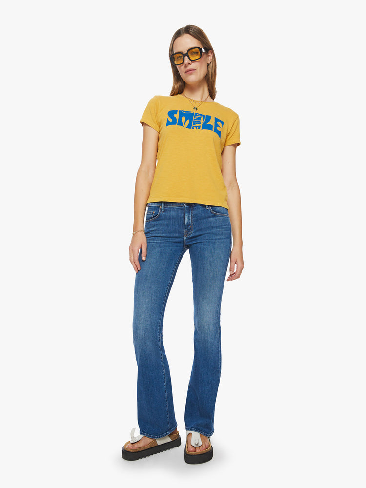 Full body  view of a woman slightly sheer crewneck in a golden yellow hue, the tee features a blue text graphic on the chest.