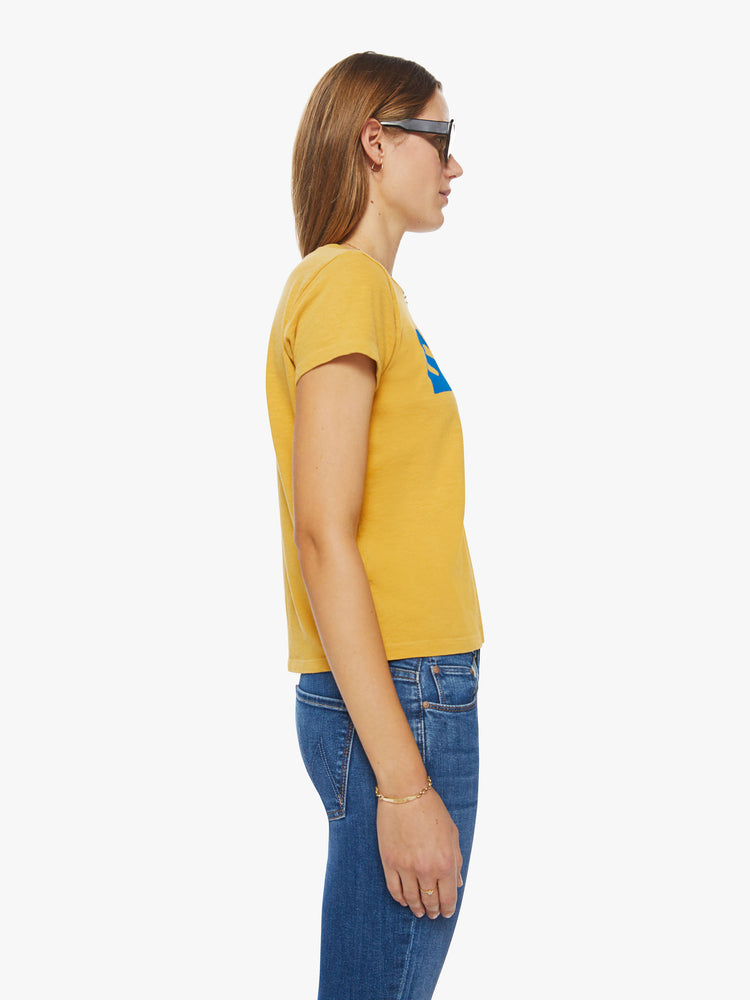 Side  view of a woman slightly sheer crewneck in a golden yellow hue, the tee features a blue text graphic on the chest.