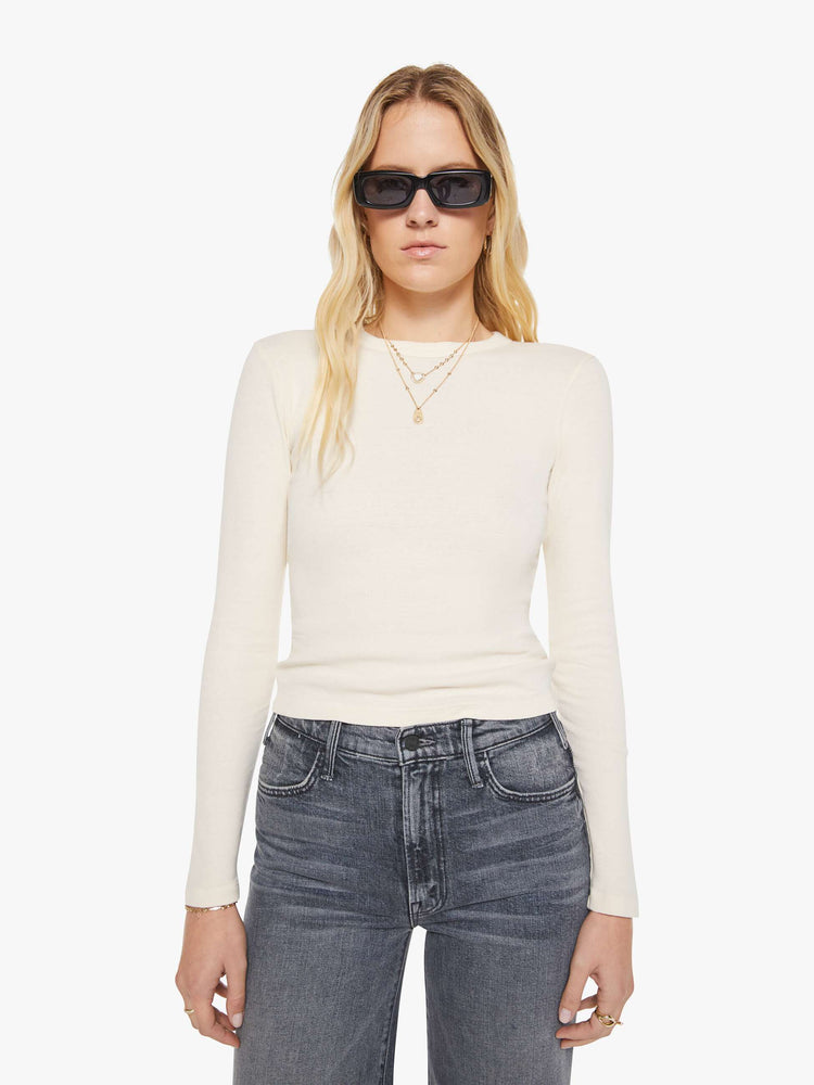 Front view of a woman in an off white crewneck top with long sleeves and a cropped fit.