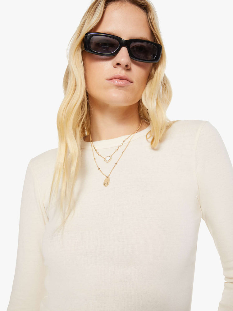 Close up view of a woman in an off white crewneck top with long sleeves and a cropped fit.