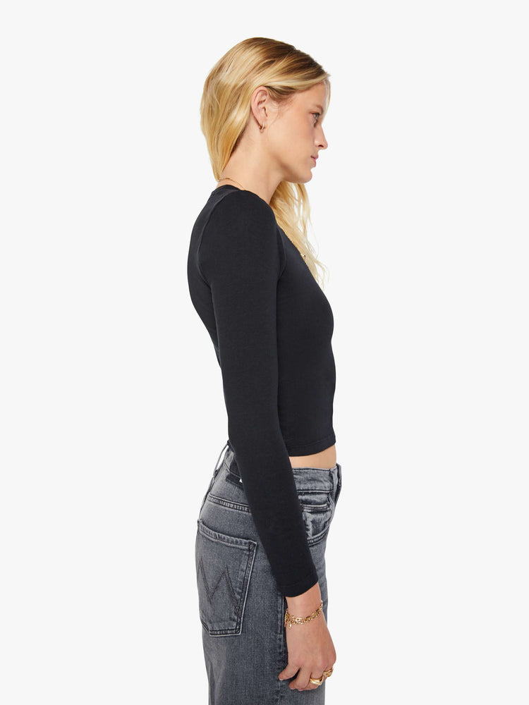 Side view of a woman in a black shrunken crewneck tee with long sleeves and a cropped length.