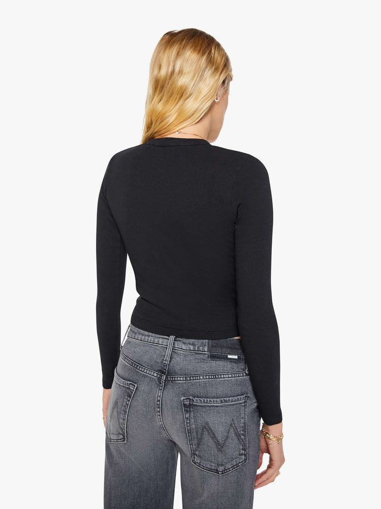 Back view of a woman in a black shrunken crewneck tee with long sleeves and a cropped length.