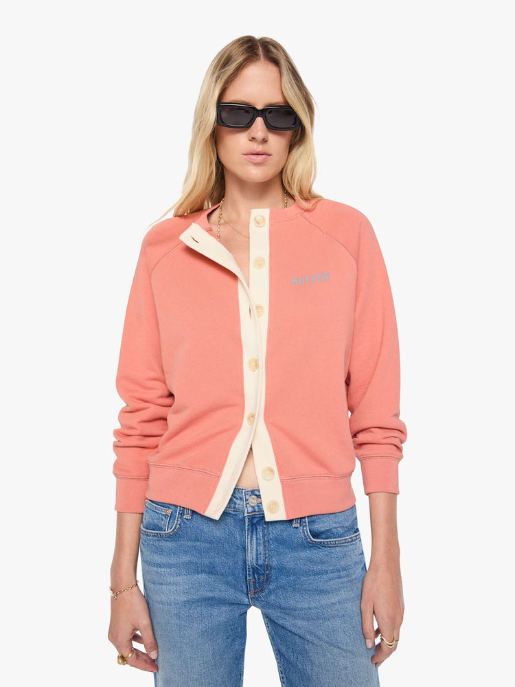 Front view of a woman  pale pink cardigan features a cream button panel and a golden tiger graphic on the back, and MOTHER's name in light blue on the chest.