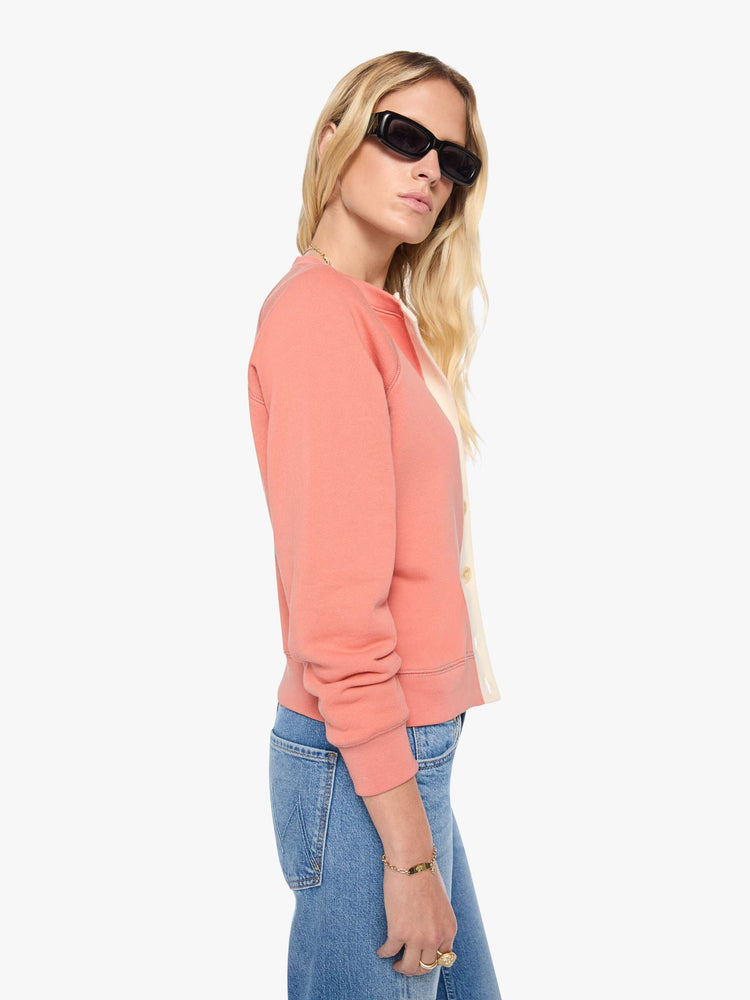 Side view of a woman  pale pink cardigan features a cream button panel and a golden tiger graphic on the back, and MOTHER's name in light blue on the chest.