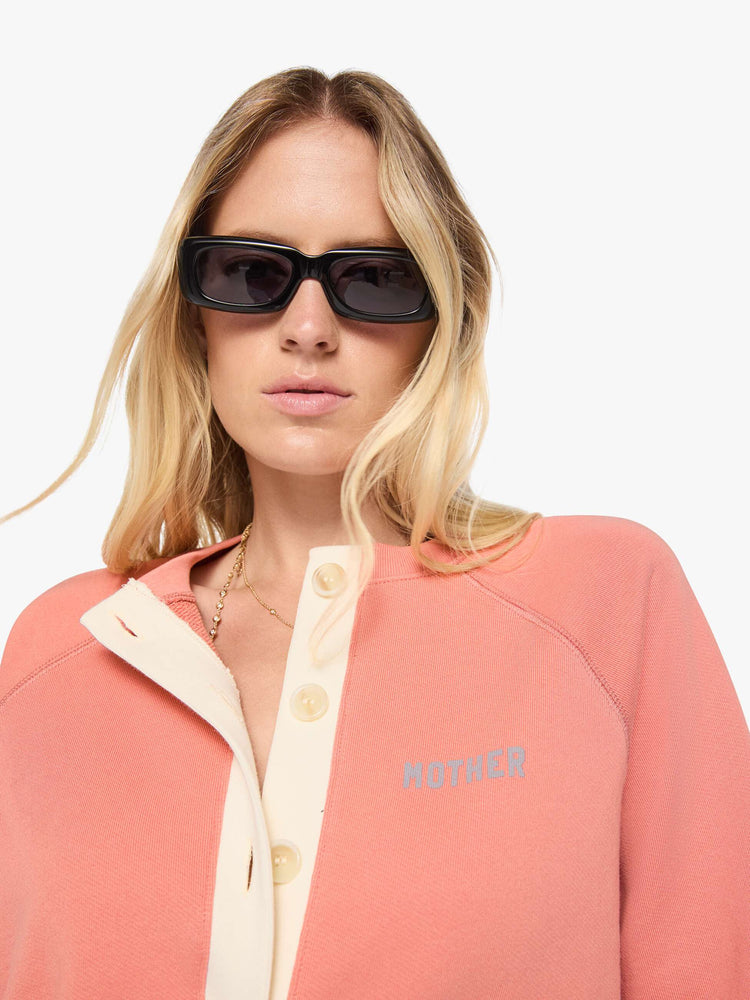 Close up view of a woman  pale pink cardigan features a cream button panel and a golden tiger graphic on the back, and MOTHER's name in light blue on the chest.