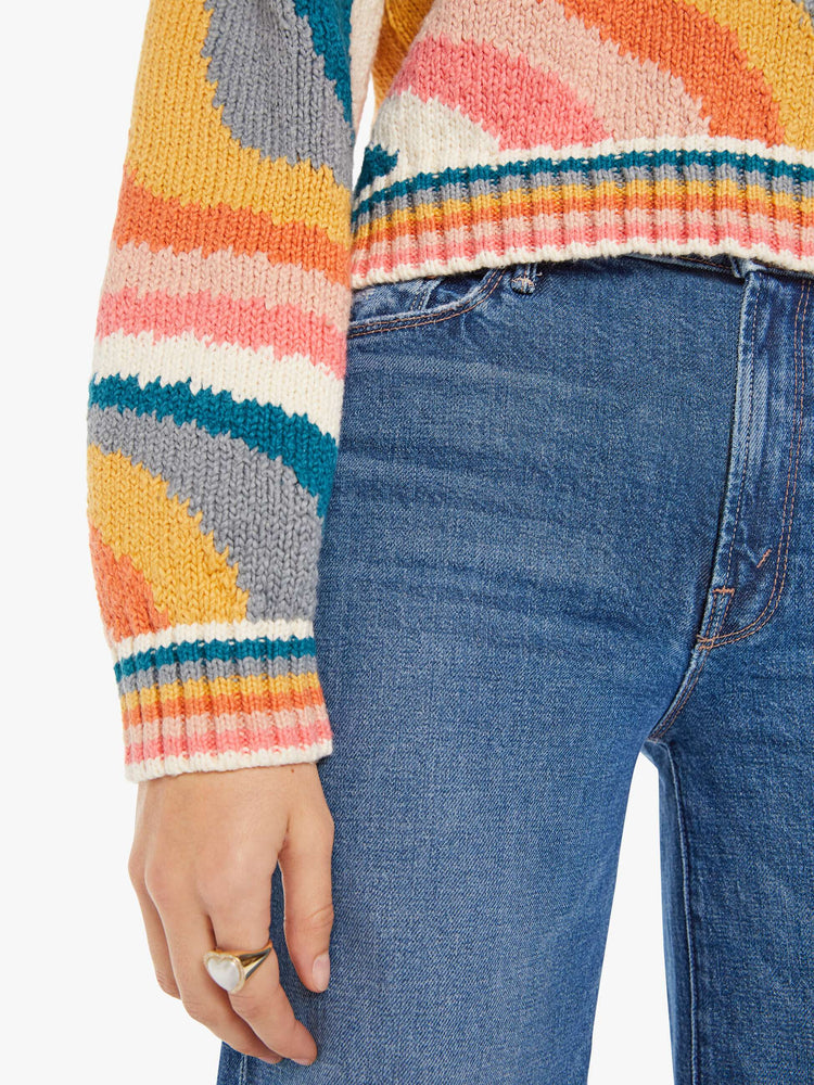 Close up detail view of a womens knit sweater featuring a boxy fit and a wavy multi color pattern.