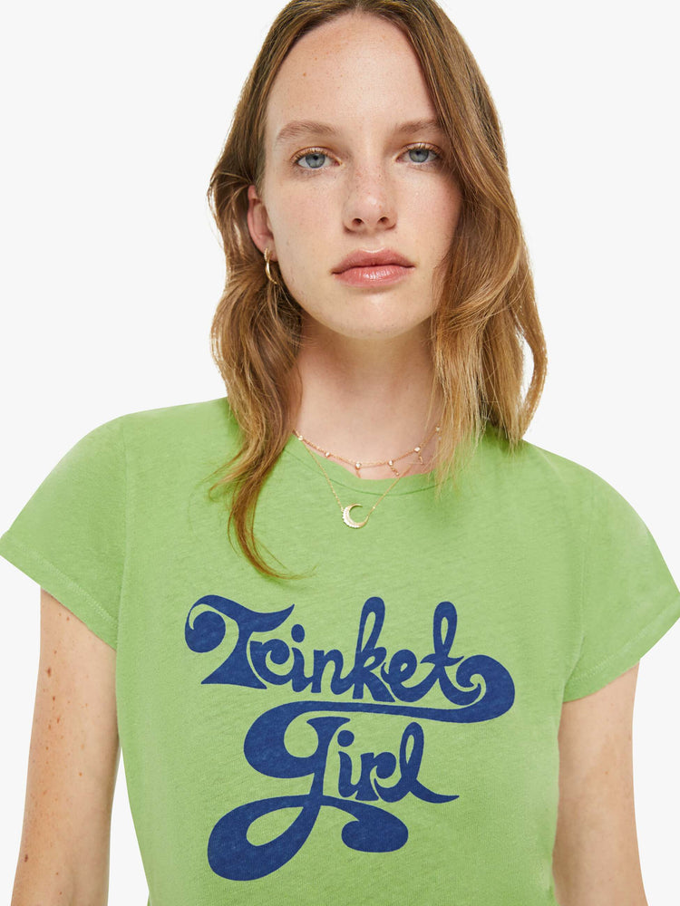 Close up view of a woman in a tee is designed in green with a blue text graphic on the front that reads "Trinket Girl."