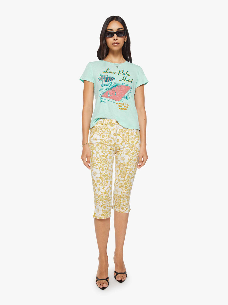 Full body view of a woman in a light teal tee with a vintage-inspired hotel logo and pool scene on the front and text in teal on the back.