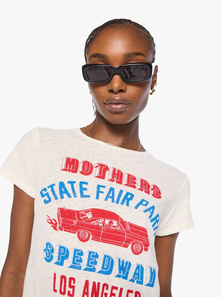 Close up view of a woman in an off-white with a vintage-inspired speedway graphic and text in red and blue on the front.