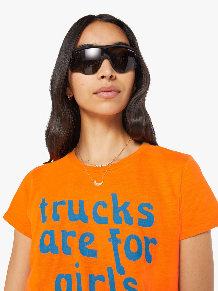Close up view of a woman in a bright orange tee with a blue graphic on the front that reads "trucks are for girls".