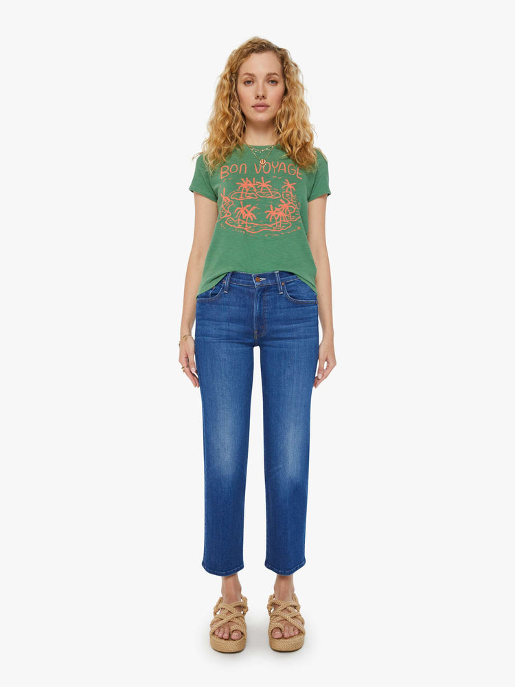 Full front view of a woman in a forest green crewneck with a slim fit featuring a hand drawn text graphic "Bon Voyage" in peach styled with blue jeans.