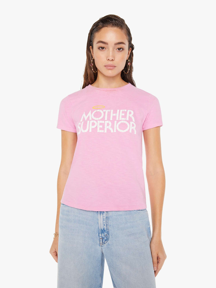 Front view of a woman wearing a fitted pink crew neck tee featuring a distressed graphic reading "MOTHER SUPERIOR" with an angel halo, paired with a light blue wash jean.