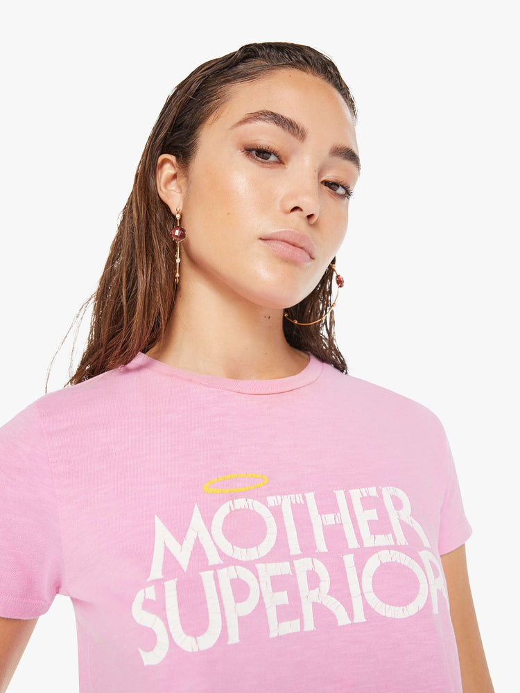Front close up view of a woman wearing a fitted pink crew neck tee featuring a distressed graphic reading "MOTHER SUPERIOR" with an angel halo.