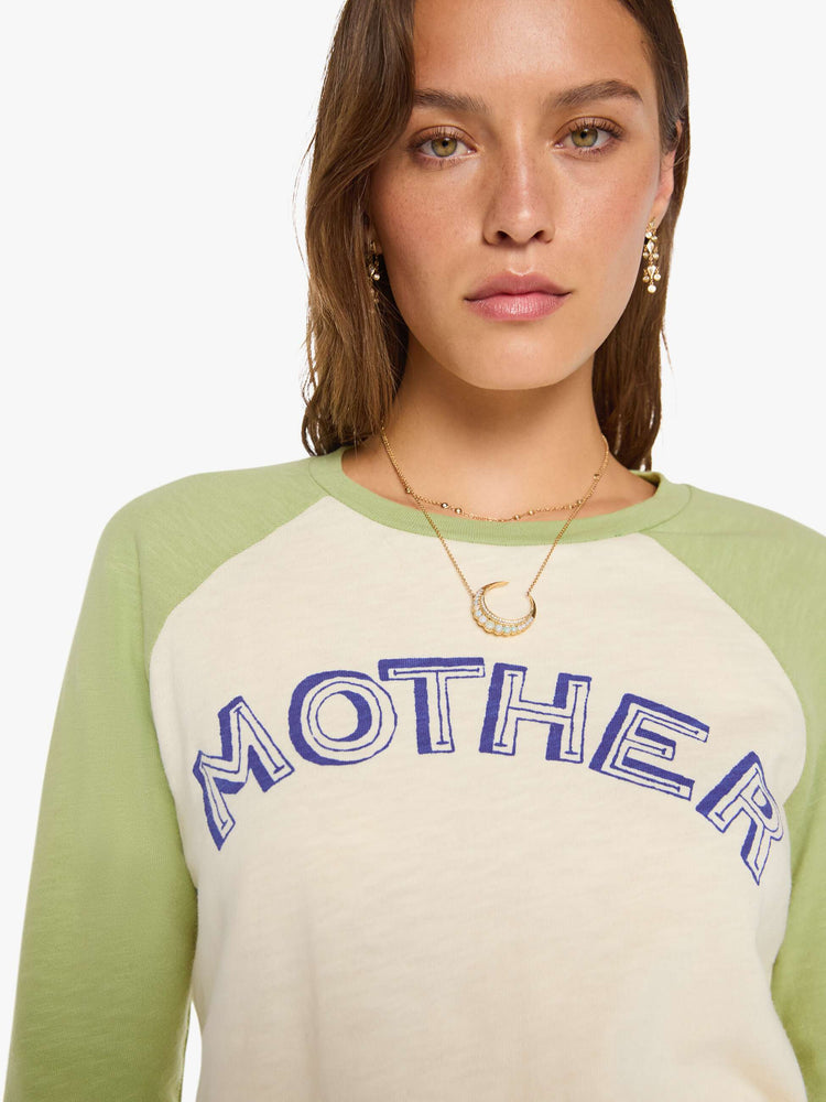 Close up view of a woman in a vintage concert tee in off-white with light green sleeves and MOTHER's name in navy block text across the chest.