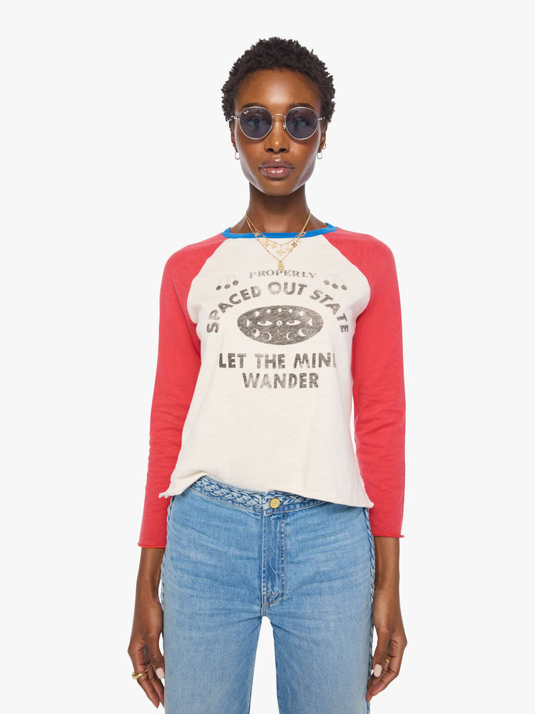 Front view of a woman in a off-white with red sleeves concert tee, blue trim and a faded celestial text graphic on the front.