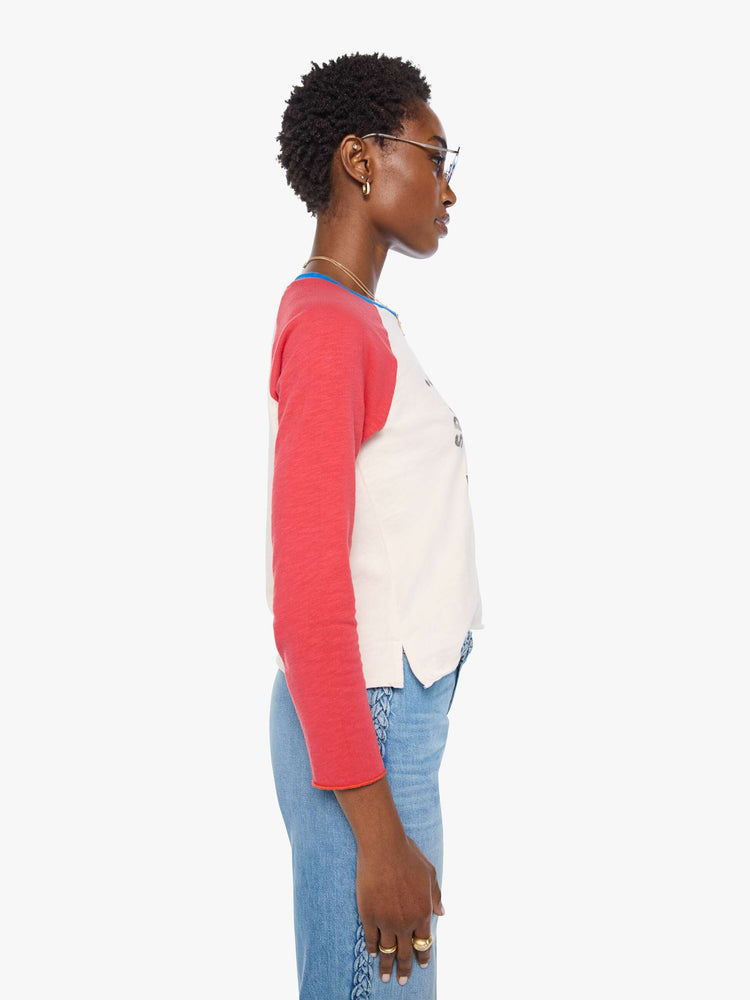 Side view of a woman in a off-white with red sleeves concert tee, blue trim and a faded celestial text graphic on the front.