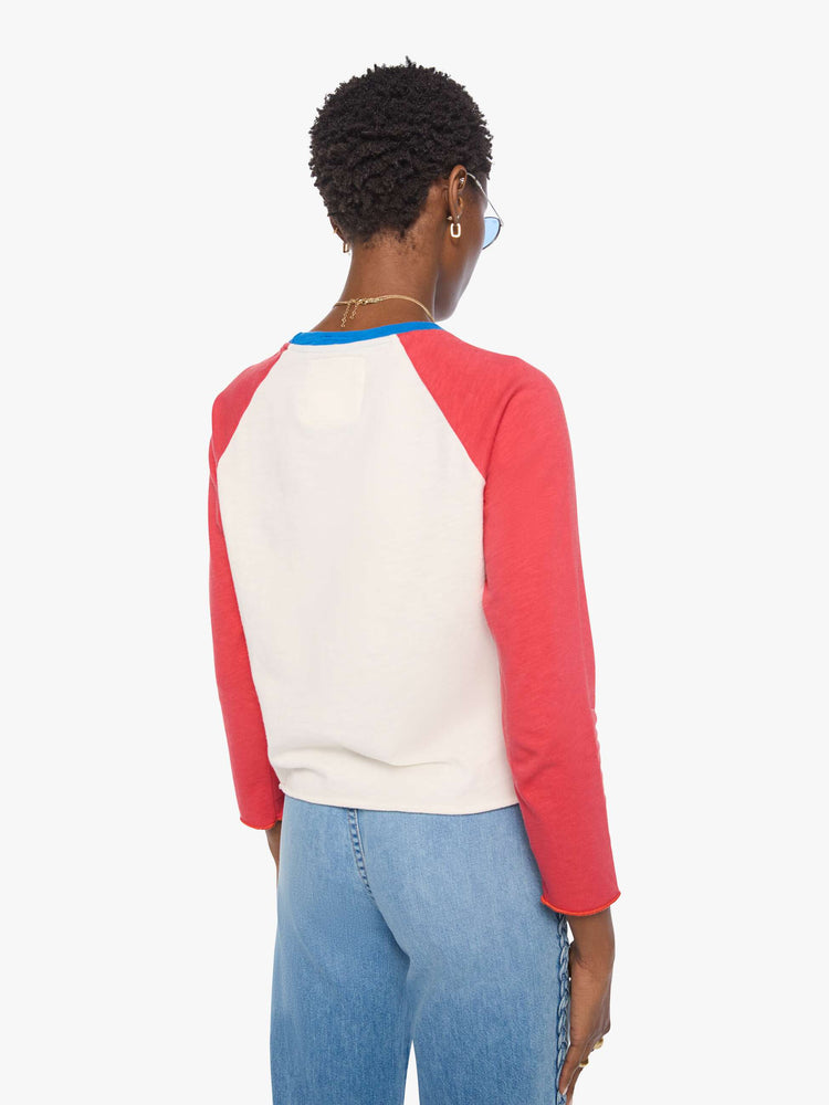 Back view of a woman in a off-white with red sleeves concert tee, blue trim and a faded celestial text graphic on the front.