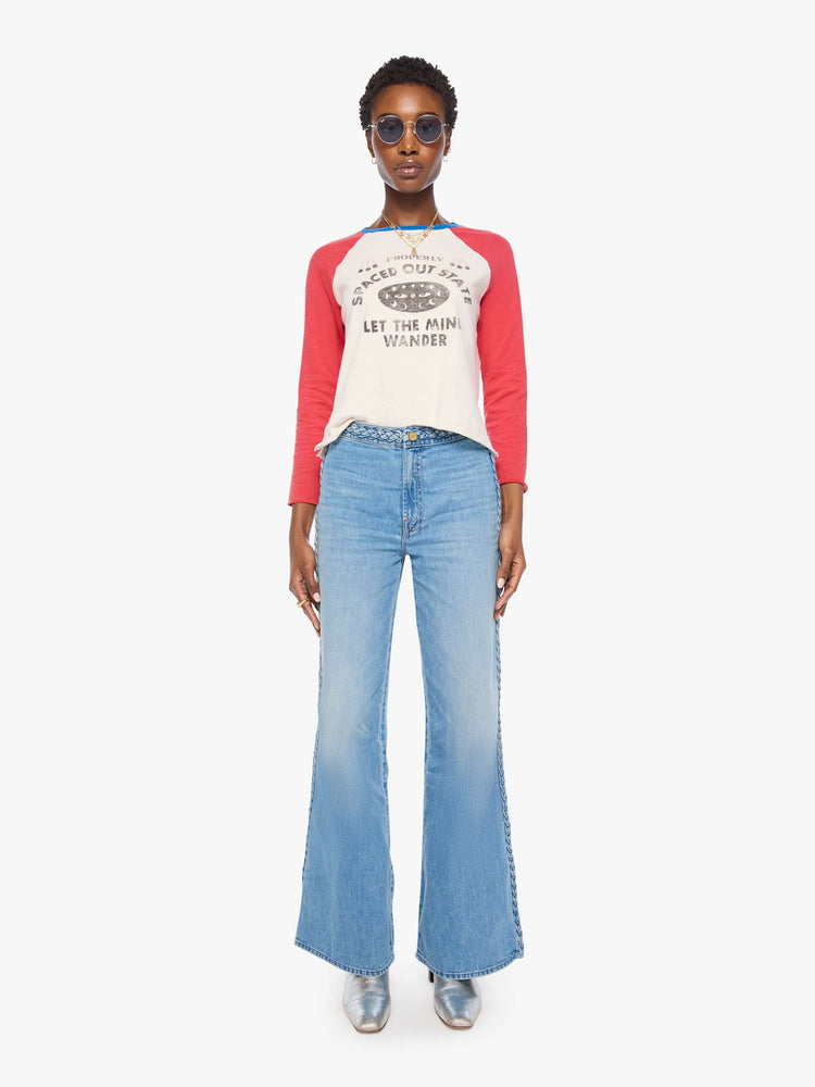 Full body view of a woman in a off-white with red sleeves concert tee, blue trim and a faded celestial text graphic on the front.