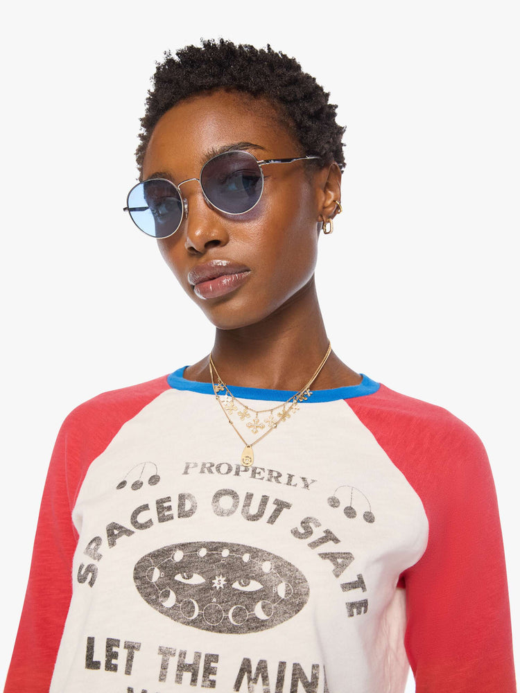 Close up view of a woman in a off-white with red sleeves concert tee, blue trim and a faded celestial text graphic on the front.