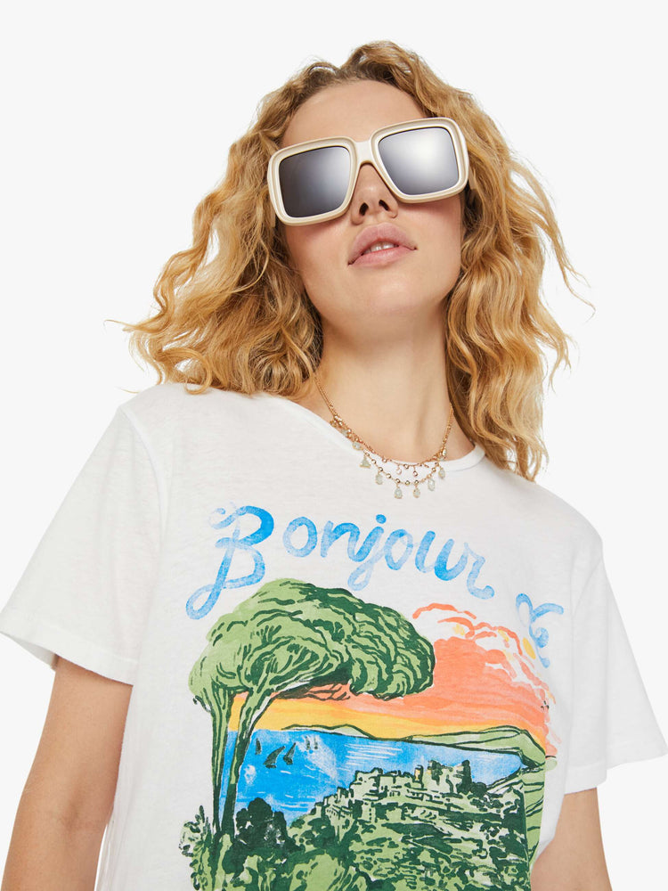 Detailed view of a woman in a white crewneck tee that features a hand-drawn seaside graphic with faded text in French on the front.
