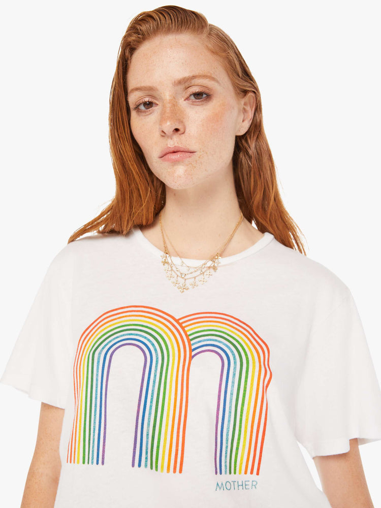 A front close up view of a woman wearing an oversized white crew neck tee featuring a large double rainbow graphic.