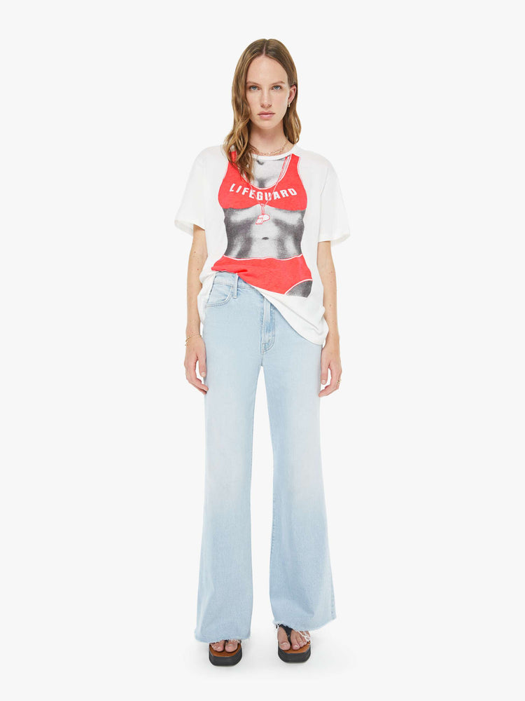 Full body view of a woman in a white tee with a black-and-white silhouette wearing an orange lifeguard bikini on the front.