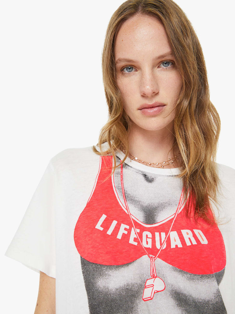 Close up view of a woman in a white tee with a black-and-white silhouette wearing an orange lifeguard bikini on the front.