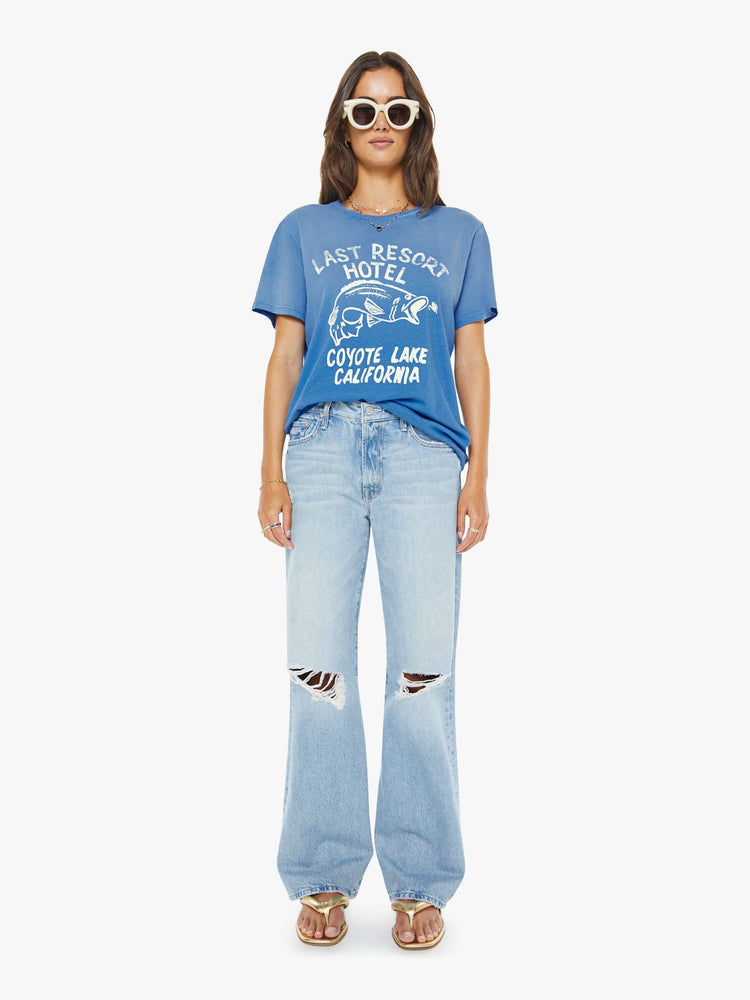 Full body view of a woman in faded blue tee with a white fish and lure graphic with text on the front.