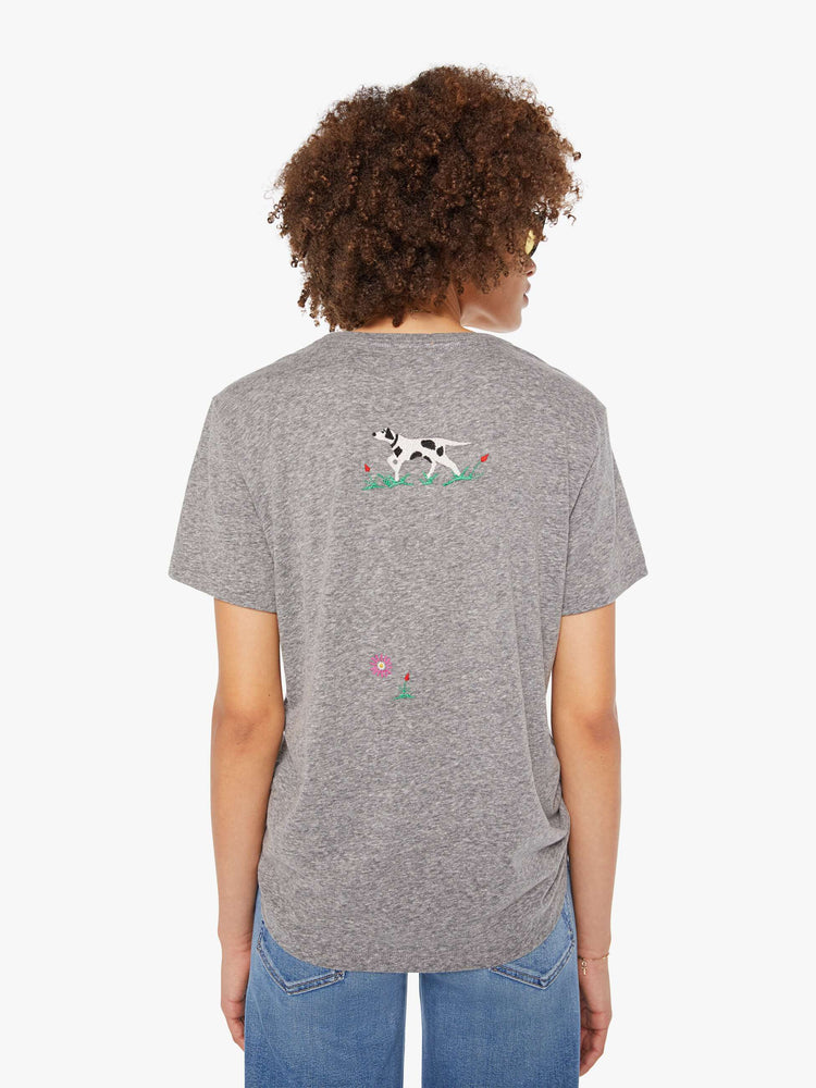 Back  view of a woman in a heathered grey tee features yellow block text on the front and colorful embroidery throughout.