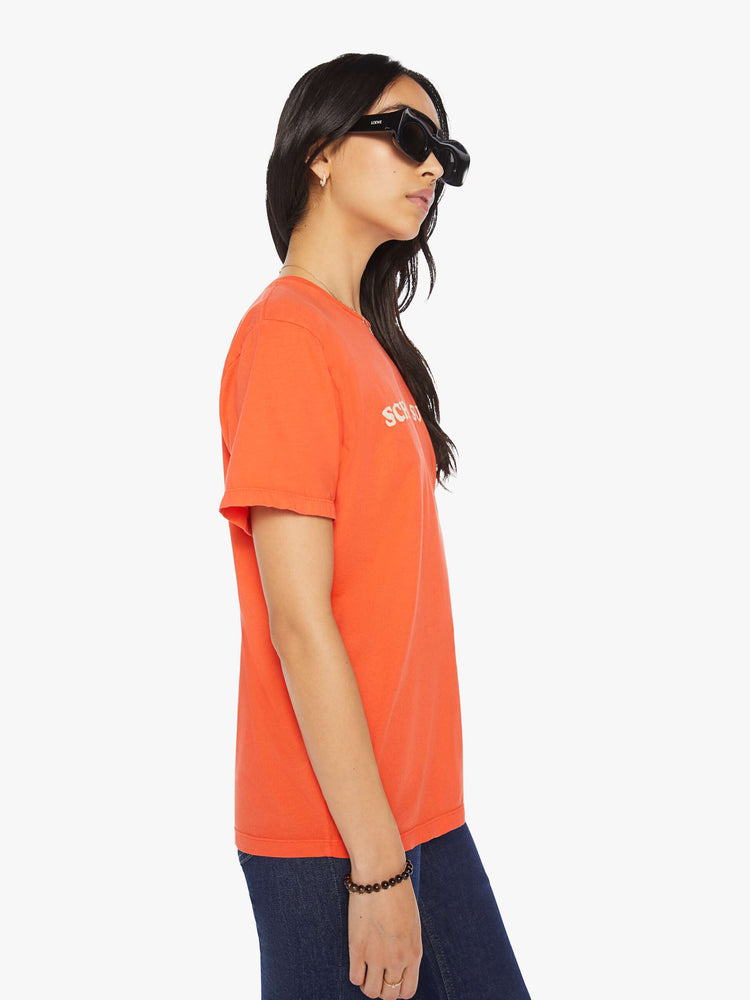 Side view of a womens orange crew neck tee featuring an oversized fit and a white graphic reading "SCHOOL SUCKS".