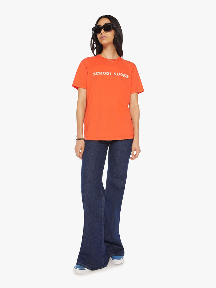 Front full body view of a womens orange crew neck tee featuring an oversized fit and a white graphic reading "SCHOOL SUCKS".