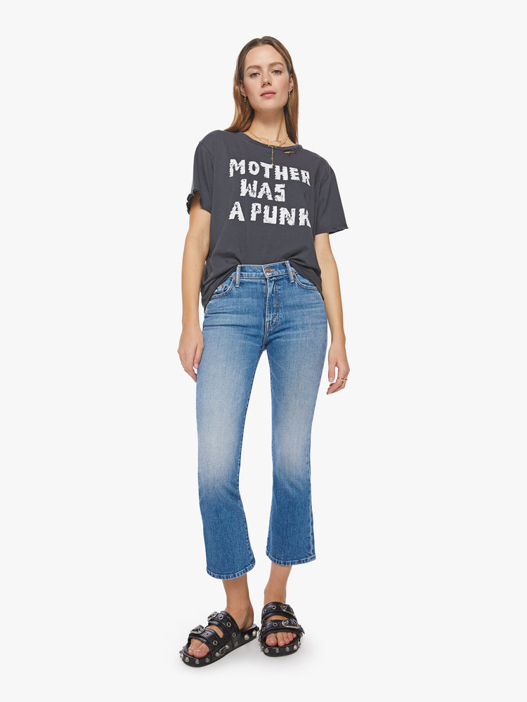 Full body view of a woman tee with an oversized fit in a faded black features a torn neckline, distressed details and a white text graphic on the front.