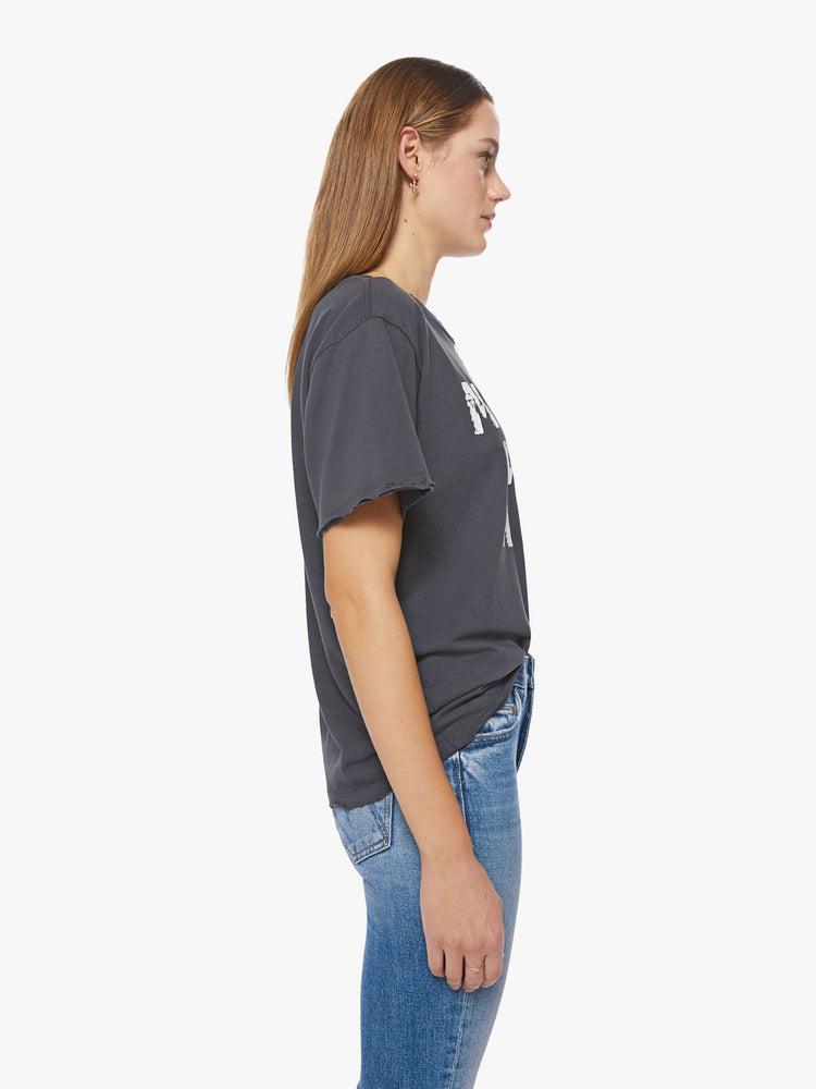 Side view of a woman tee with an oversized fit in a faded black features a torn neckline, distressed details and a white text graphic on the front.