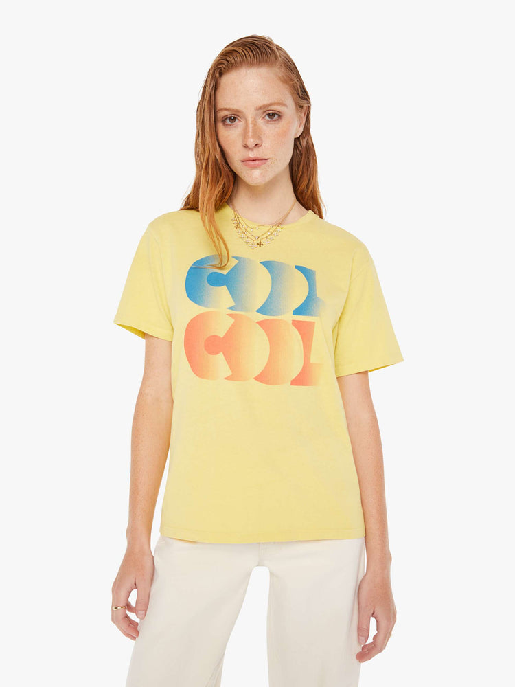A front view of a woman wearing a faded yellow oversized crew neck tee featuring a red and blue graphic reading "COOL COOL", paired with off white jeans.