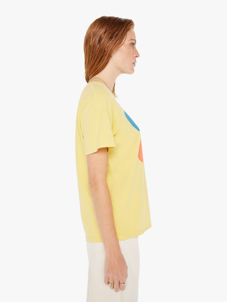 A side view of a woman wearing a faded yellow oversized crew neck tee featuring a red and blue graphic reading "COOL COOL", paired with off white jeans.