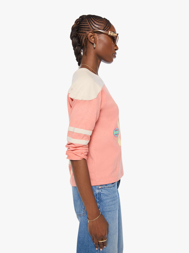 Side view of a long sleeve pale pink with an off-white panel across the shoulders, horizontal stripes on the sleeves, the number 15 in cream on the front and colorful sewn patches throughout.