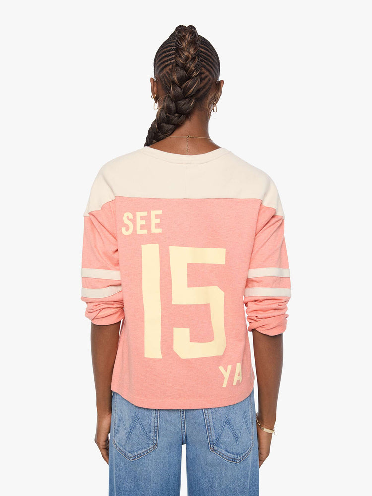 Back view of a long sleeve pale pink with an off-white panel across the shoulders, horizontal stripes on the sleeves, the number 15 in cream on the front and colorful sewn patches throughout.