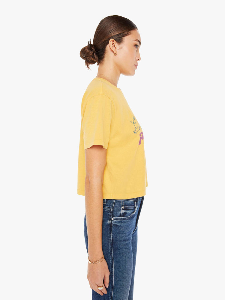 Side view of a womens yellow crew neck tee featuring a boxy, cropped fit and a graphic of a woman and "pour quoi?" in purple.