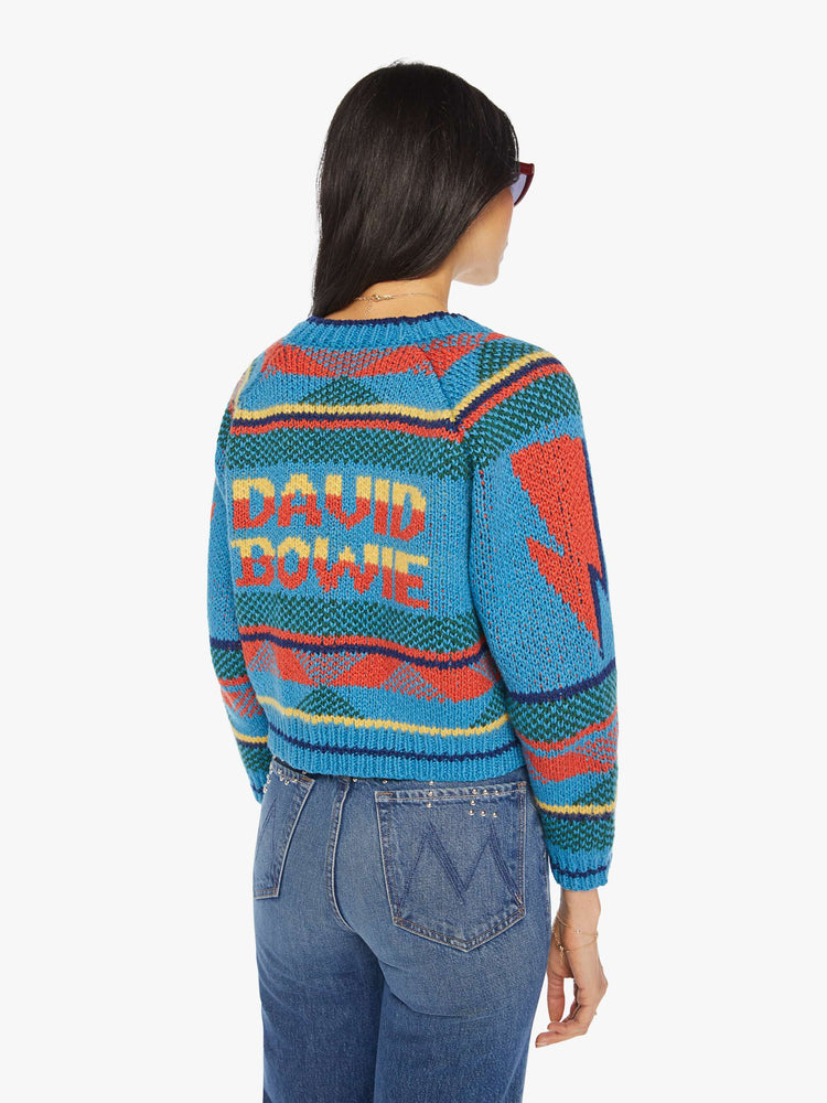 Front view of a womens blue knit cropped cardigan featuring a colorful pattern, a lightning bolt down the arm sleeve, and "DAVID BOWIE" across the back.