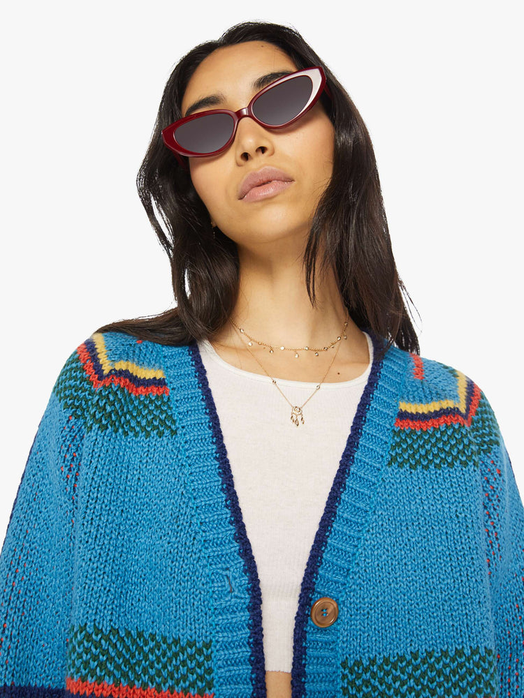 Front close up view of a womens blue knit cropped cardigan featuring a colorful pattern.