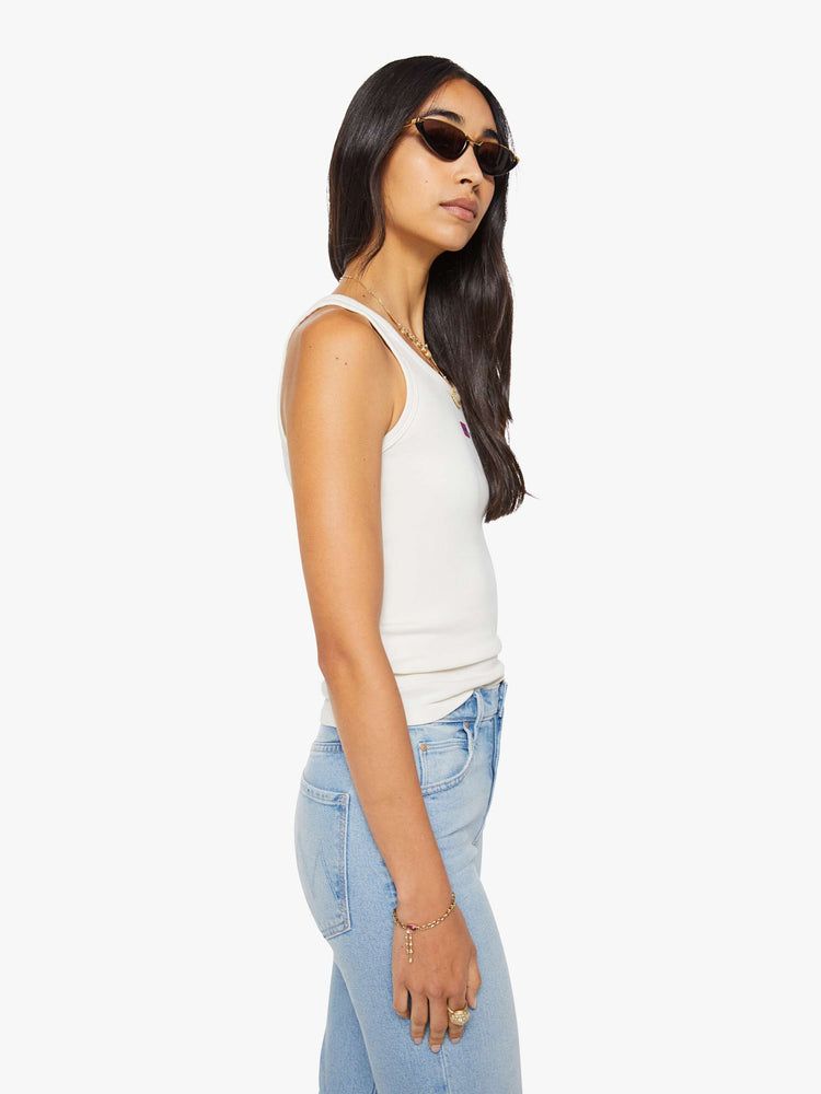 Side view of a woman in a white with fire cracker tank with wide straps and a slightly shrunken fit.