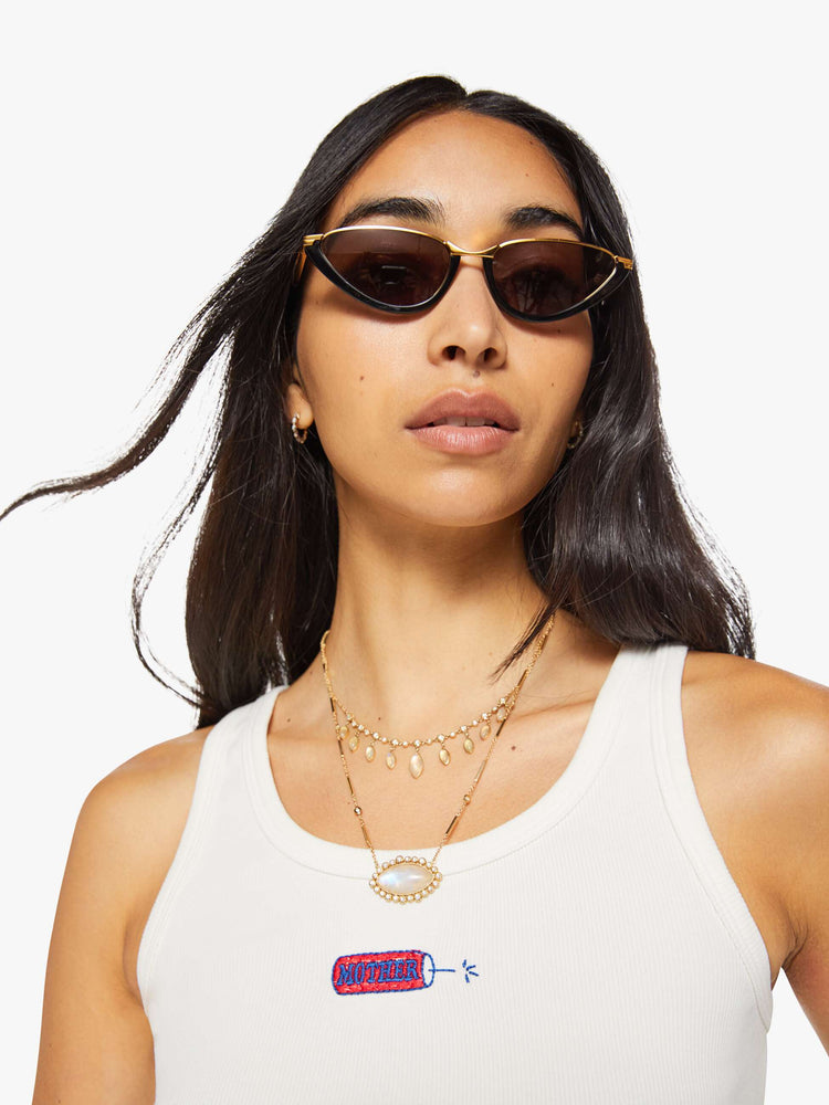 Close up view of a woman in a white with fire cracker tank with wide straps and a slightly shrunken fit.
