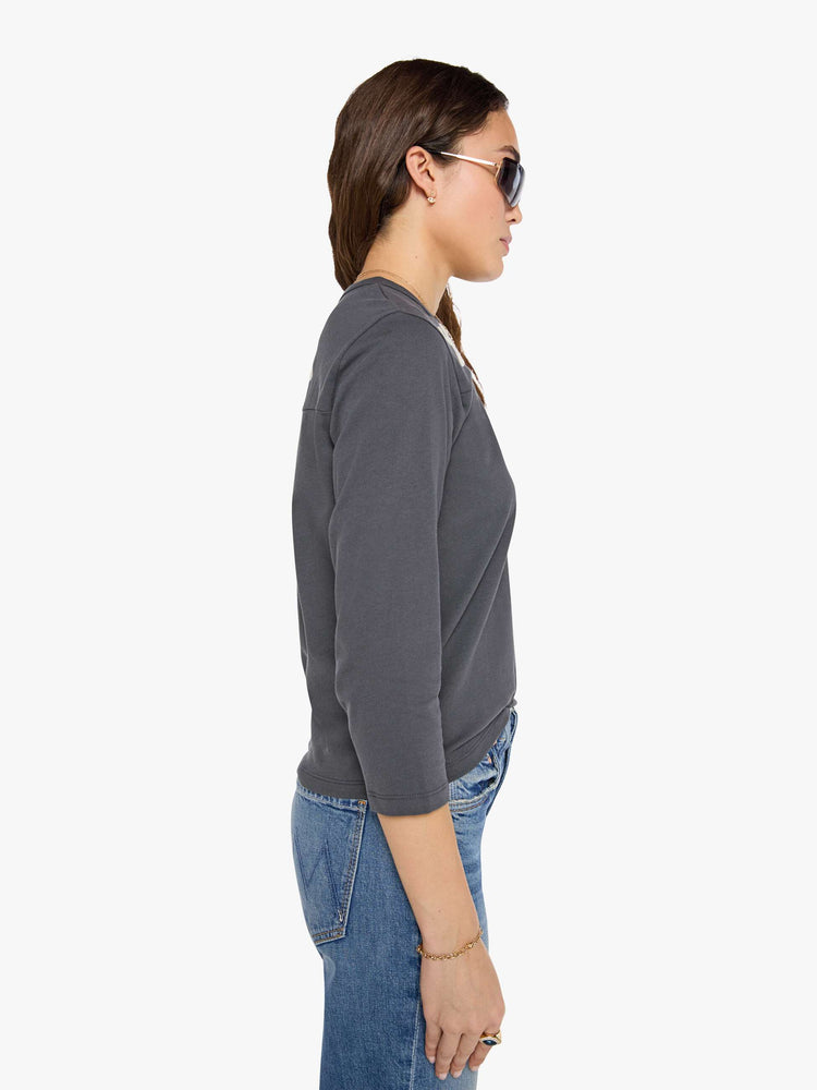 Side view of a woman in a faded black top designed with a 26 patch on the chest, ROCK across the back, and MOTHER's name embroidered in yellow at the hip.