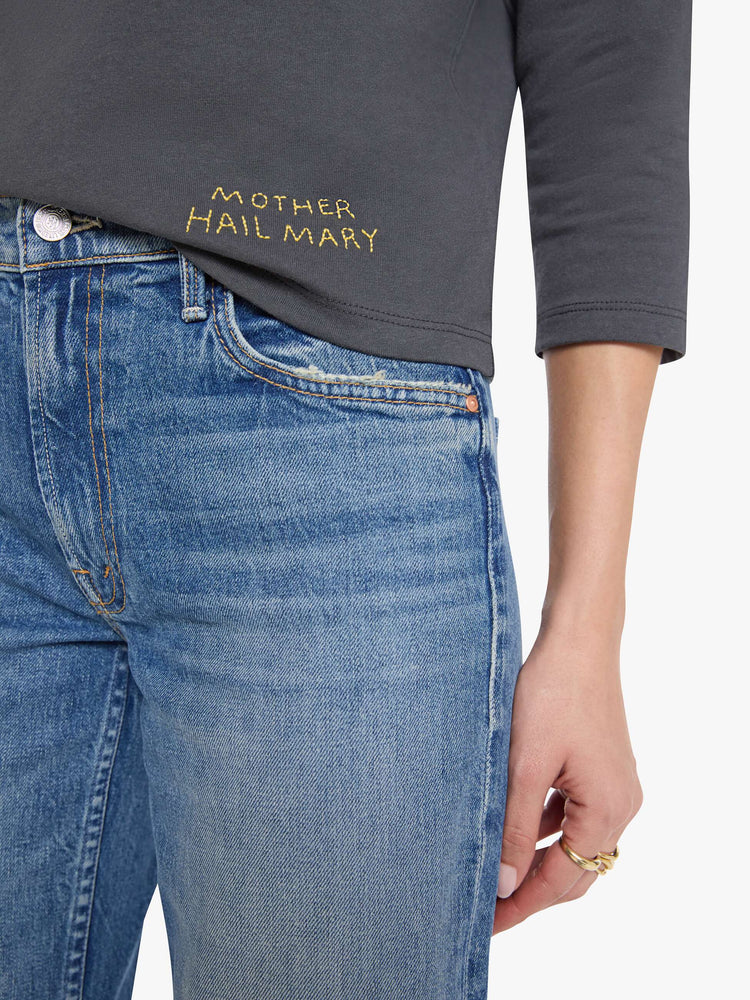Close up view of a woman in a faded black top designed with a 26 patch on the chest, ROCK across the back, and MOTHER's name embroidered in yellow at the hip.