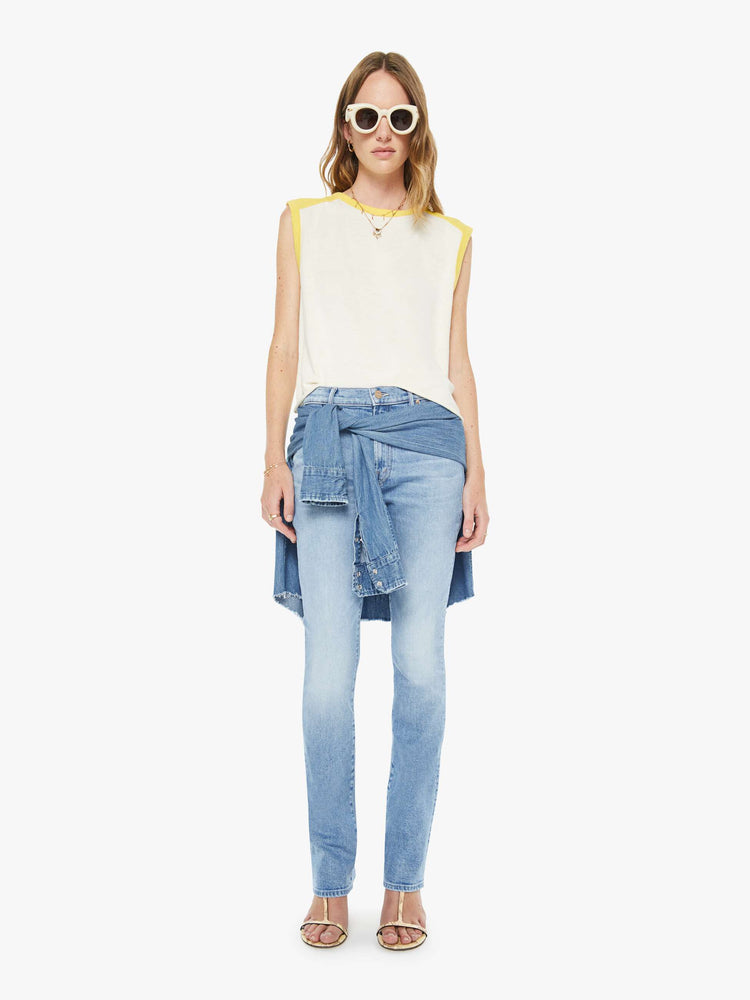 Full body view of a woman in an off-white  tee with cutoff sleeves and a raw hem. 