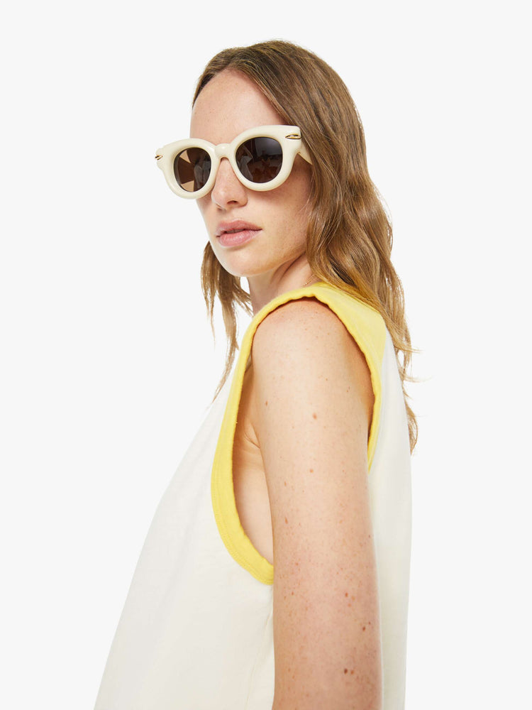Close up view of a woman in an off-white  tee with cutoff sleeves and a raw hem. 
