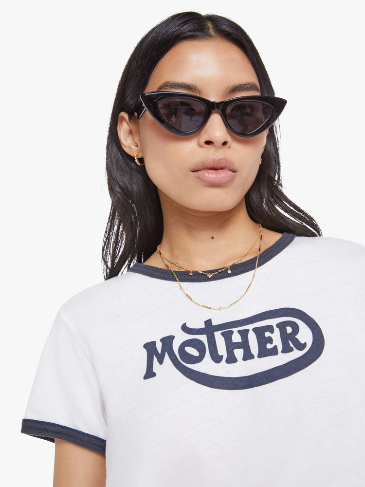 Close up view of a woman in a white tee with navy trim, the tee features MOTHER's name on the front.