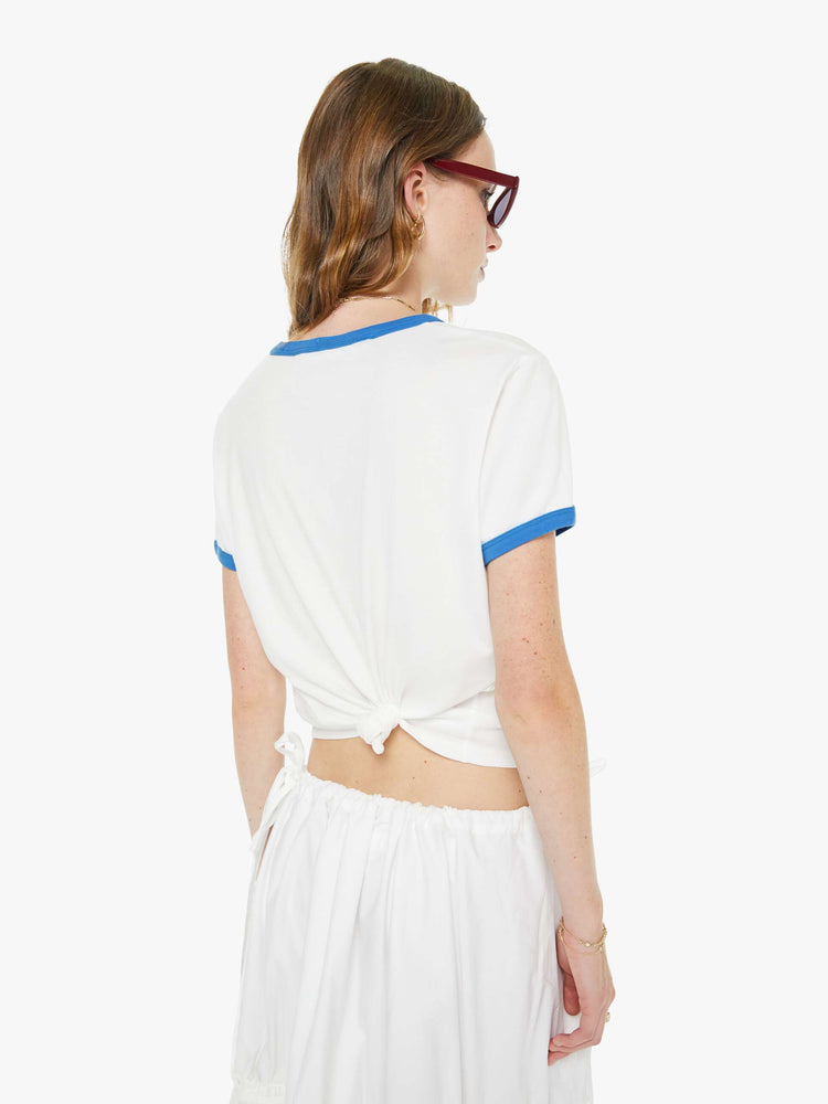 Back view of a woman in off-white with light blue trim tee and a colorful text graphic inspired by a vintage scoreboard on the front.
