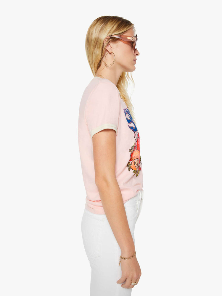 Side view of a woman in a light pink with cream trim tee with extra-short sleeves and a slightly shrunken fit.