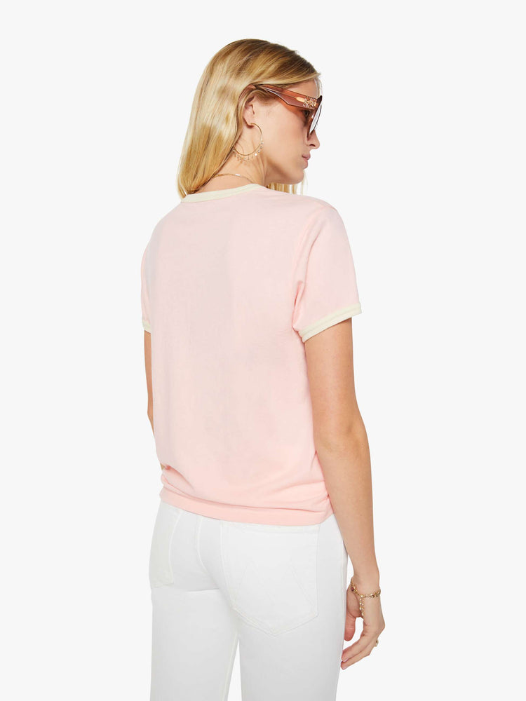 Back view of a woman in a light pink with cream trim tee with extra-short sleeves and a slightly shrunken fit.